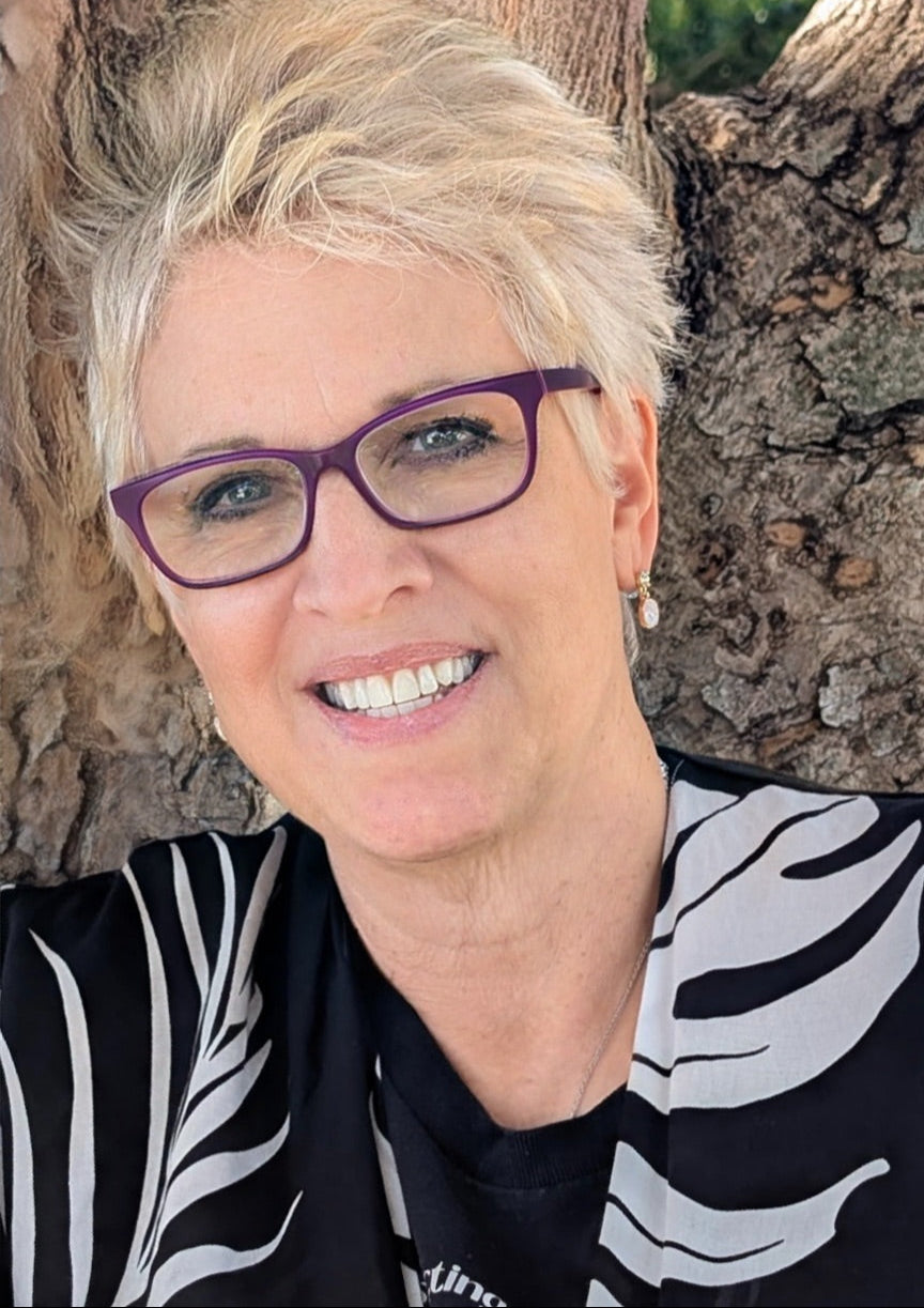 Person wearing purple glasses and a black and white patterned shirt against a tree background
